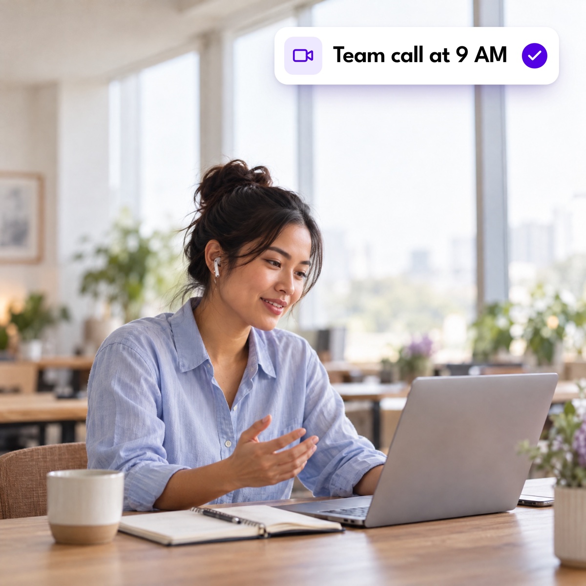 A woman on a video call at her laptop in a bright office, with a "Team call at 9 AM" notification