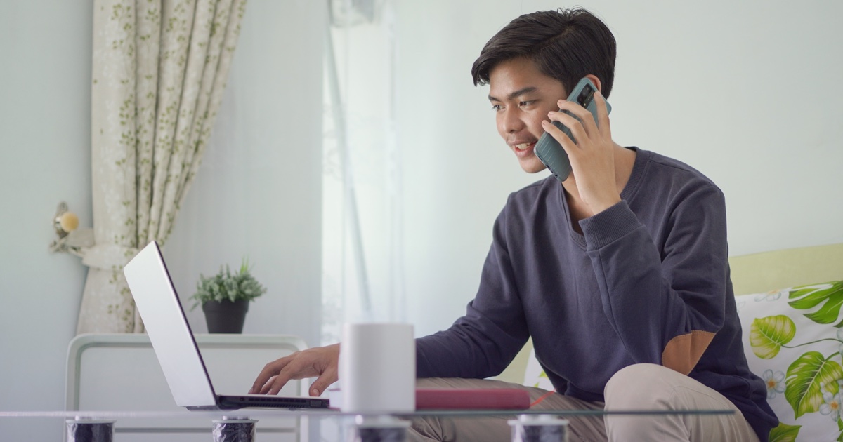 A professional speaks on the phone while working at a laptop.